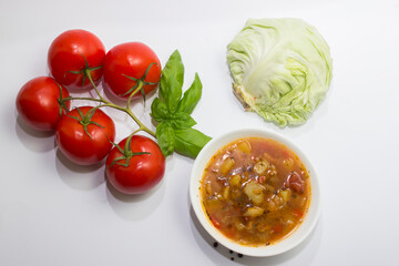 Cabbage and tomato soup with chicken. White background. Next to the ingredients