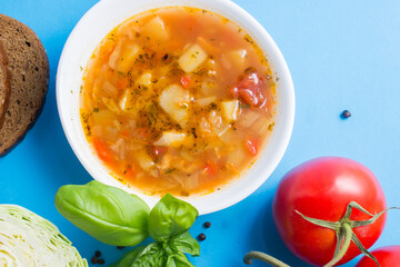 Cabbage and tomato soup with chicken.blue background. Next to the ingredients