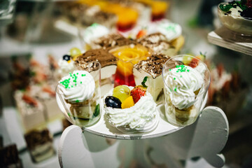 Close up of tray with lot delicious diversity pastry cakes tartlets and macaroon in a row. Fresh, multicoloured, colourful, green, yellow, white and pink sweet berry desserts, beautifully decorated