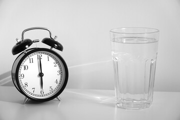 Clear glass of water for drinking on bed in the morning. An image of a retro clock showing 6:00 am....