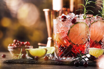 Red alcohol cocktail with cranberries, ice and rosemary on wooden background, copy space