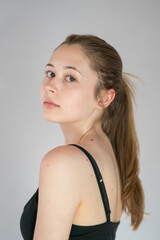 Semi profile portrait of a languishing and charming young woman with ponytail hair posing looking at the camera on a grey background