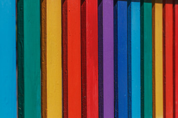 Part of a bright wooden fence painted in rainbow colors on a warm summer day in the park. Joyful mood in the decor.