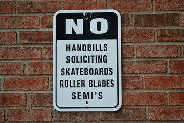 A Black and White Sign on a Brick Wall Stating "No Handbills Soliciting Skateboards Roller Blades SEMI'S"