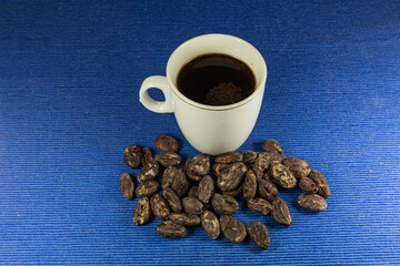 Coffee cup and saucer on wooden table. Dark blue background. Close up dark roasted fair trade coffee beans. Top view.