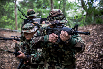 Fototapeta premium Team of army soldier with machine gun moving in the forest,Thai militia soldier in combat uniforms in the wood,Wander the patrol sloping in the rainforest.