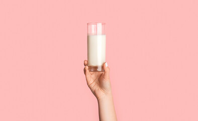 Cropped view of female hand holding glass of fresh milk on pink background