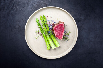 Gegrilltes dry aged Wagyu Filletkopf beef fillet head Medallion Steak vom Rind mit grünen Spargel  und Kräuter als Draufsicht auf einem Modern Design Teller mit Textfreiraum
