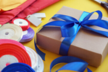 Gift box packaging on a yellow background. A lot of bright satin ribbons.