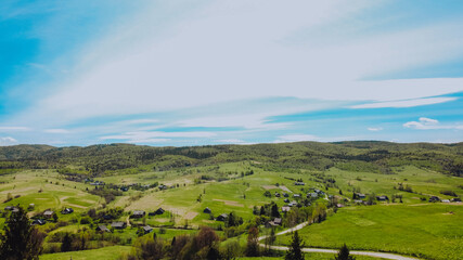 Obraz premium Aerial view to the small ukrainian village in the mountains with some beautiful fields, green grass and mountains at the background. 