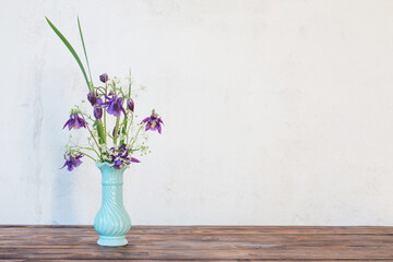 flowers in vase on wooden table on background white wall