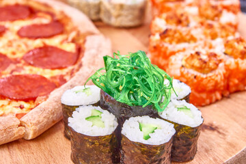 Pepperoni pizza with sushi rolls set on wood