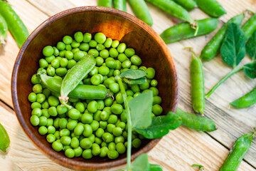 closeup green peas in brown dish, on wooden table.
