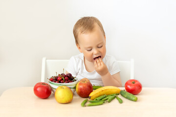 baby boy 2 years old sitting at a table on a white isolated background and eating fruits vegetables, baby food concept, place for text