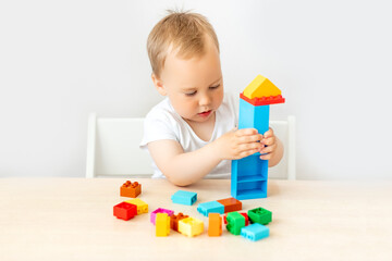 child a boy 2 years old sits at a table on a white isolated background and collects a constructor, early development, a place for text