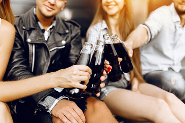 Stylish young students relaxing and drinking drinks in glass bottles, sitting in the city center, on the pavement