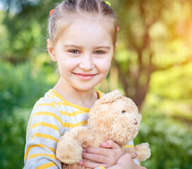 Portrait of cute smiling little child girl with her favorite teddy bear toy at the park in summer