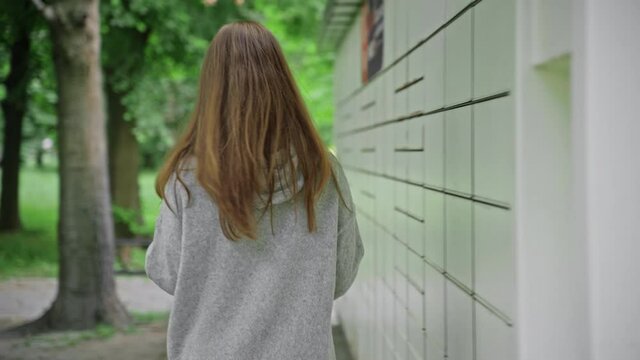 Woman in protective mask and gloves during coronavirus COVID-19 pandemic picks up delivery package at parcel locker using smartphone
