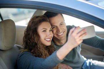 Young couple sitting in the car, making selfie and smiling