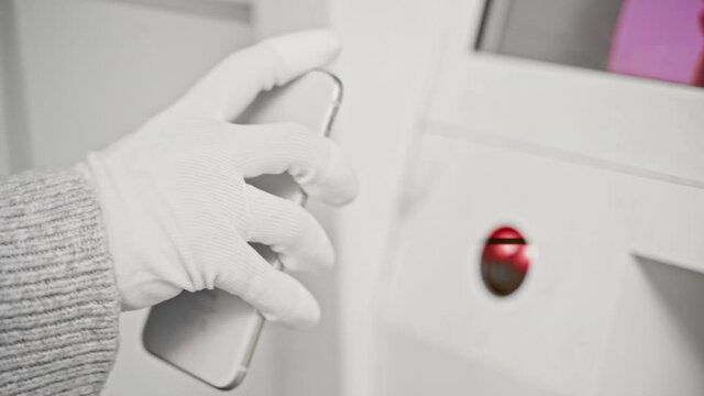 Woman in protective mask and gloves during coronavirus COVID-19 pandemic picks up delivery package at parcel locker using smartphone