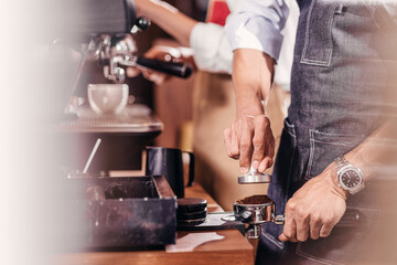 Fototapeta na wymiar Closeup Asian Barista tamping the portafilter and preparing cup of coffee for espresso with latte or cappuccino for customer order in coffee shop