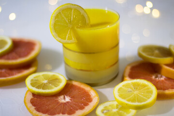 A glass of orange juice with distant citrus fruits on a white background