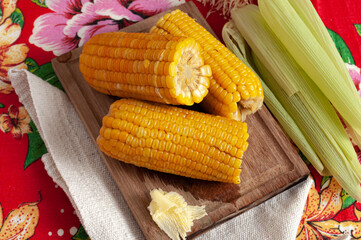 cooked corn with butter on wooden board and colorful table