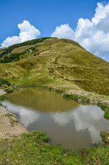 Fototapeta na wymiar Mountain Lake in the high Carpathian mountains of Ukraine with clouds and green pasture in summer