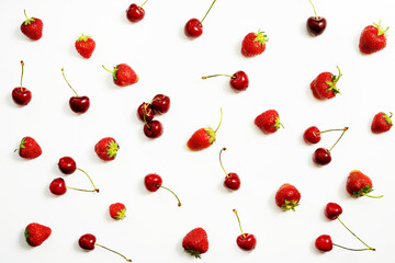 Berries of ripe strawberries and cherries are scattered on a white table. Top view.