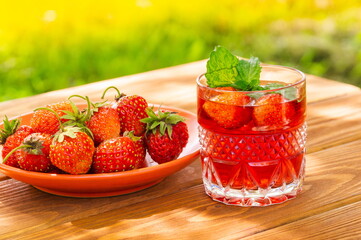 Strawberries in plate on the table and fresh drink with mint on a sunny day