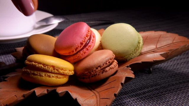 Female hand takes a French almond macaroon from a leaf-shaped plate on the background of coffee cup