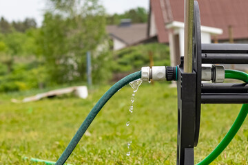 Daylight. in focus the fitting drips water from it. Near a hose reel