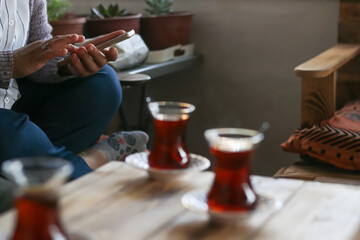 Young lady viewing mobile phone in her hand and standing at the table with glasses full of fresh tea.