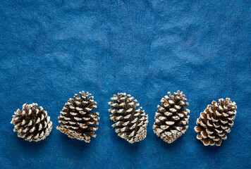 row of frosty decorative pine cones against blue textured bark paper with a copy space, winter holidays concept