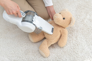 Woman vacuuming furniture in a house with a hand-held portable vacuum cleaner.