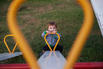 A small boy looking at camera in aplayground, sitting on a seesaw