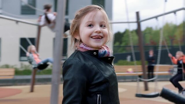 Little child blond girl having fun outdoors on children playground. Stock footage. Beautiful blond caucasian girl smiling while walking in the street.