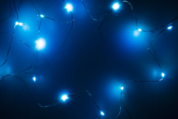 Top view of garland on wooden background in dark. Christmas backdrop with blue lights, copy space.