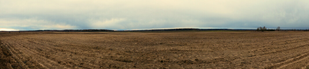 Plowed field on a cloudy evening. Agro-industrial landscape. Panorama.