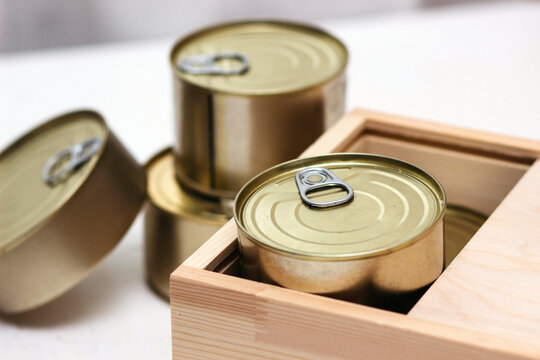Tin cans in a box. A variety of canned food in full tin cans. Real canned food. View from above. Selective focus.