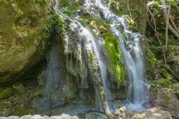Fototapeta premium Beautiful jungle waterfall between mossy rocks. Long exposure shot, motion photo. Wild nature, national park. Hiking, traveling.