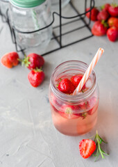 Strawberry lemonade with rosemary and ice in mason jar on a gray concrete table. Seasonal food concept. Summer harvest time, top view