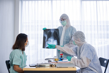 Naklejka premium Asian doctor in personal protective equipment or ppe explain the x-ray film of covid-19 or coronavirus infection to patient in the hospital. coronavirus, covid-19 outbreak, or medical hospital concept