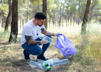 Volunteer man collecting plastic bottles in a forest, in garbage bag, ecology