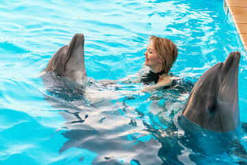 Beautiful young happy girl laughs and swims with dolphin in the pool