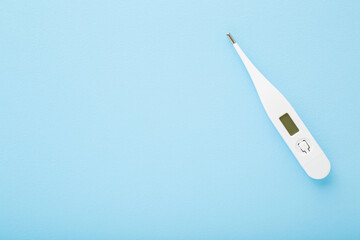 White digital thermometer on light blue table background. Pastel color. Fever and healthcare concept. Closeup. Empty place for text. Top down view.