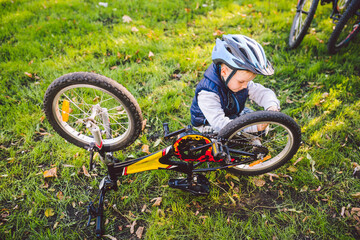Active leisure for children in the park. A child is studying the mechanism of a mountain bike. Toddler fixing a bike in the forest. Cycling club for children. Little bicycle mechanic at work