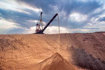 Industrial background. Salt mining site under a sky with dramatic clouds. Large excavator machine and Huge mountains of waste ore in the extraction of potassium.