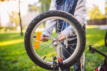 Active leisure for children in the park. A child is studying the mechanism of a mountain bike. Toddler fixing a bike in the forest. Cycling club for children. Little bicycle mechanic at work