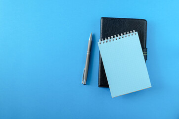 Fototapeta na wymiar A daily planner or e-book in a black leather cover, a notepad and a pen on the blue surface. Horizontal orientation. View from above, copy space.
